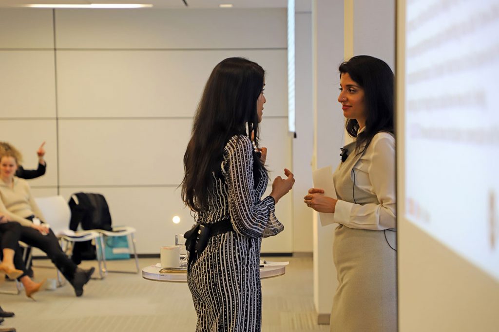 Ritu Bhasin and Dr. Komal Bhasin having a conversation next to a projector screen in a conference room