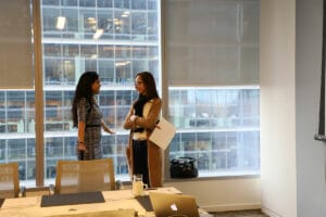 Ritu Bhasin speaking to a woman in business attire in front of a window in a conference room