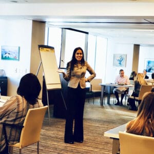 Ritu Bhasin standing next to a flip chart while presenting to a conference room of people