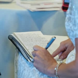 The lap of a woman sitting at a table holding a notepad on her lap writing notes with a pen