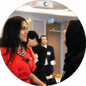 Ritu Bhasin standing in a busy conference room in conversation with a smiling woman wearing a hijab