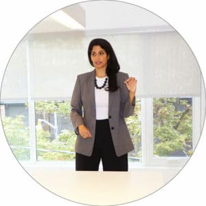 Dr. Komal Bhasin stands at the end of a table in front of some windows teaching