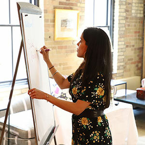 Profile view of Ritu Bhasin in a conference room writing on a flip chart with a marker