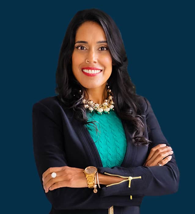 Ritu Bhasin standing with her arms crossed and smiling on a navy background