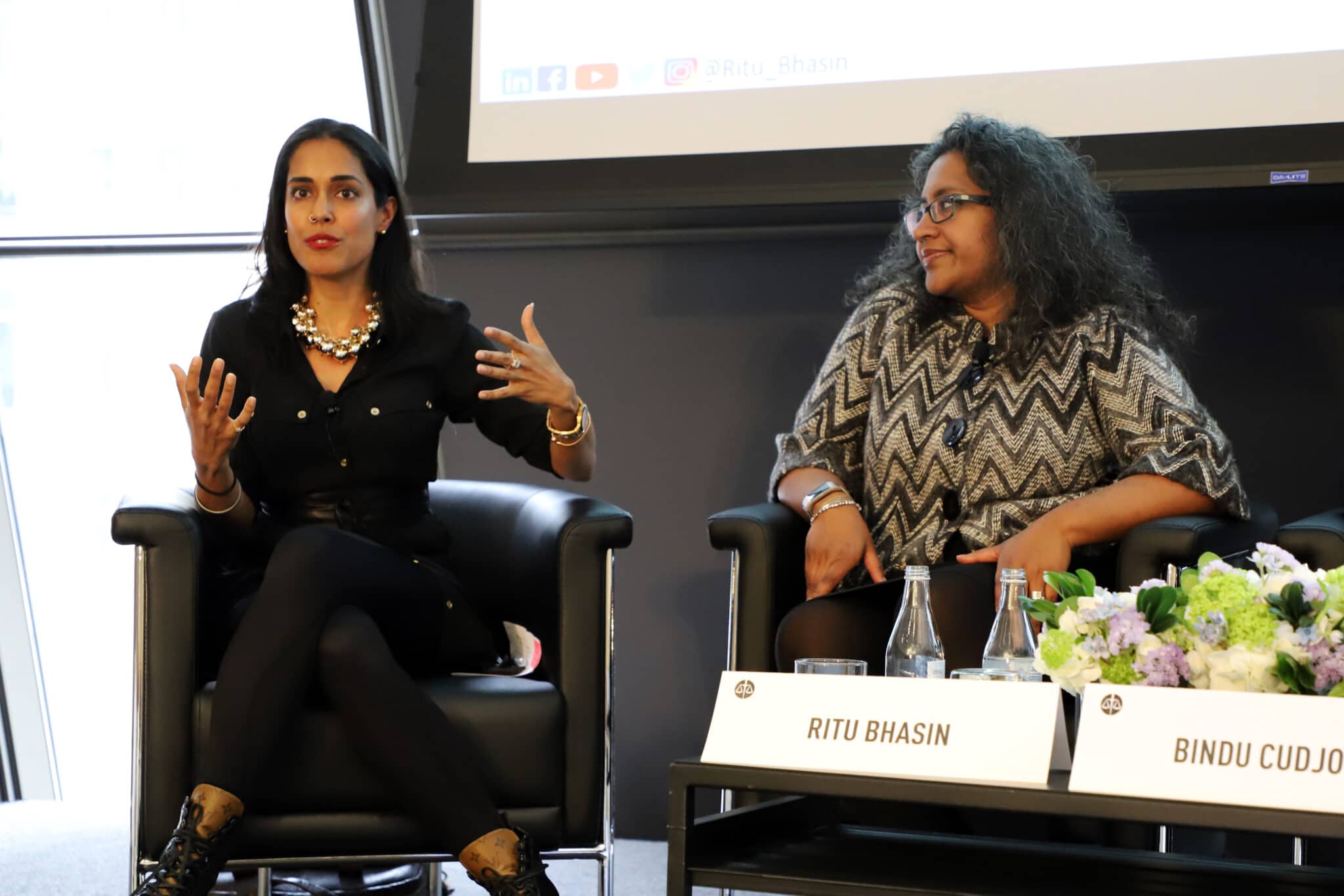 Ritu Bhasin sitting onstage in a chair speaking to an audience next to another woman of color as part of panel discussion
