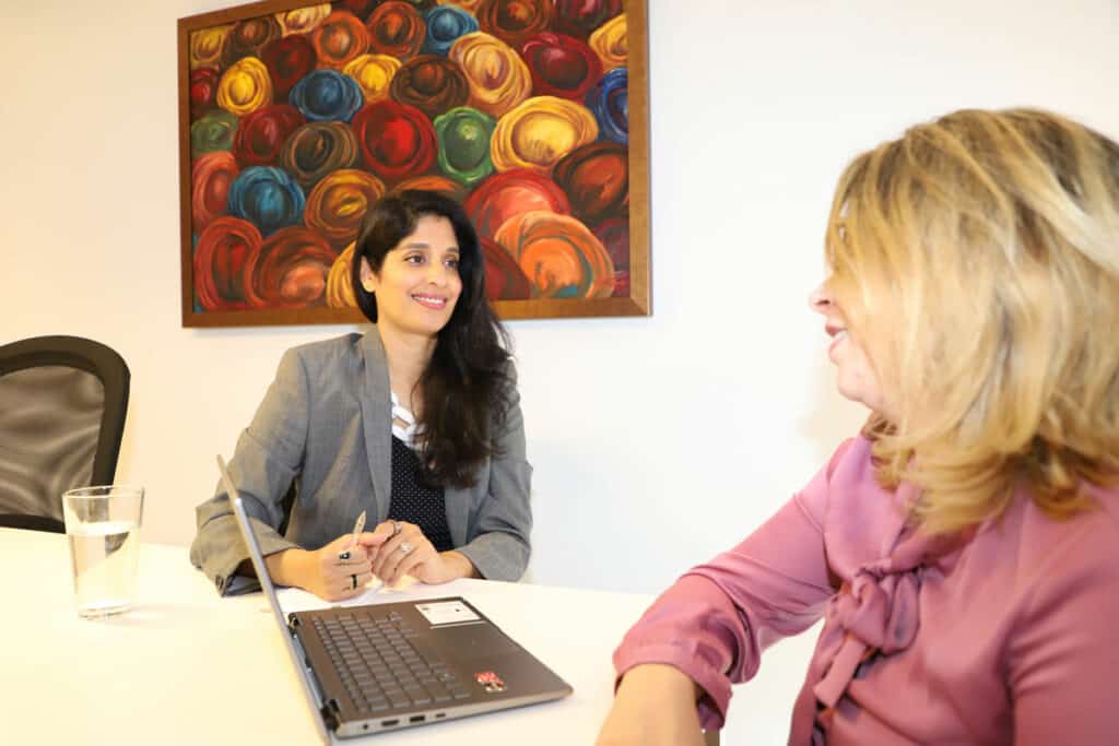Dr. Komal Bhasin sits at a table across from a woman with blonde hair who has a laptop computer open in front of her