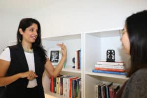 Dr Komal Bhasin speaking to a young woman with black hair in front of a white bookshelf